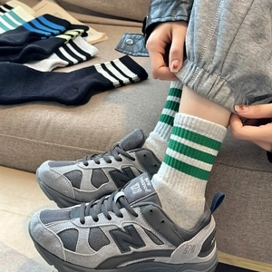 Detail of grey crew socks with green stripes styled with athletic sneakers on feet