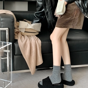 Detail of grey ribbed wool socks paired with black plush slippers for cozy winter fashion