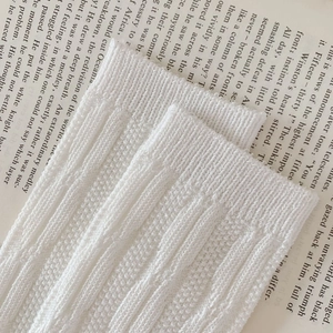 Detailed view of white knitted cotton sock cuff with vertical ribbing texture on a book