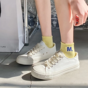 Detailed shot of yellow cotton sports socks with blue M embroidery worn with white sneakers
