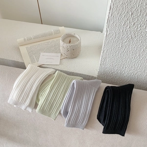 Close-up of ribbed knit socks in white, green, and grey on a cozy minimalist background