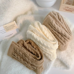 Close-up of three knitted neck warmers in brown, beige, and khaki with chunky cable knit texture