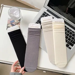 Set of four ribbed cotton mid-calf socks in black, grey, and cream on an office desk