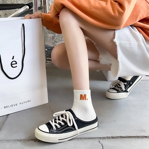 Detail of white cotton socks with orange M embroidery paired with black canvas mule shoes