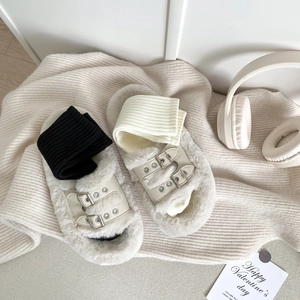 White faux fur slides with dual metal buckle straps on a cozy home setting background