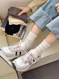 Close-up of ribbed cotton crew socks in cream, black, and coffee colors worn with sneakers