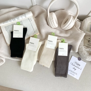 Flat lay of ribbed crew socks in white, black, beige, and grey with cozy lifestyle props