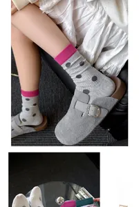 Détail de chaussettes grises à pois avec bords roses et mules en daim à boucles argentées