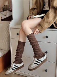 Dettaglio di scaldamuscoli in maglia marrone con trama a coste retrò abbinati a scarpe