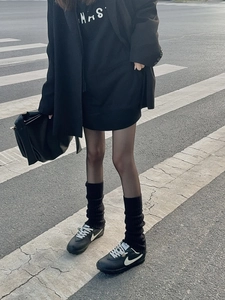 Scaldamuscoli neri a maglia abbinati a sneaker e gonna su una strada cittadina