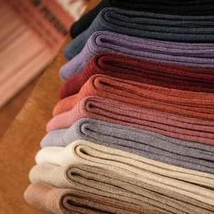 Detail showing various colors of ribbed cotton socks stacked on a wooden surface