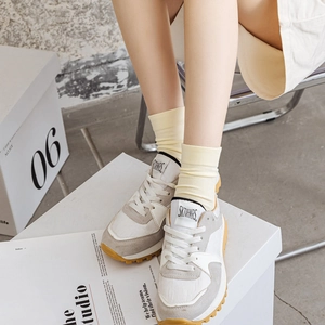 Detail of beige and grey sneakers featuring a bold yellow lugged rubber sole on foot