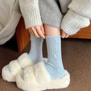Detail of wool socks with heart embroidery and color flecks worn with plush slippers