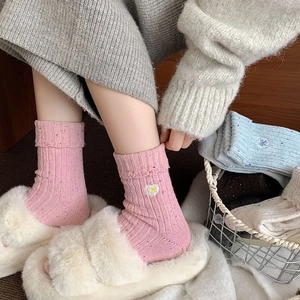 Detailed embroidery of heart and bow on pink wool socks with colorful speckled yarn texture