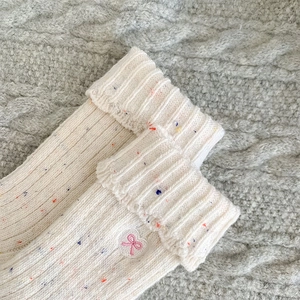 Detail of cream rib-knit wool socks with rainbow flecks and pink heart bow embroidery