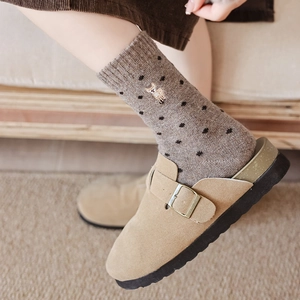 Close-up of wool socks with polka dots and deer embroidery worn with khaki suede clogs