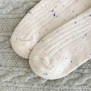 Macro shot of knitted wool sock toe with colorful neps and ribbed texture in beige