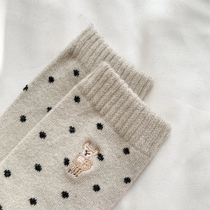 Close-up of wool socks featuring black polka dots and a cute alpaca embroidery detail