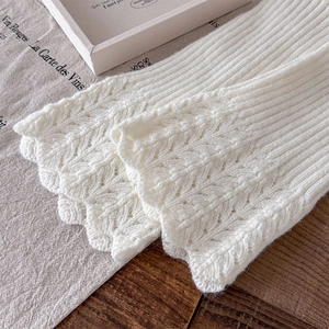 Détail de jambières en tricot blanc avec motif losange ajouré et bordure festonnée élégante