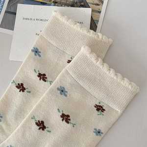 Detailansicht cremefarbener Stricksocken mit blauen Blumenstickereien und Rüschenrand