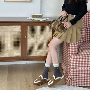 Detail of dark grey ribbed socks paired with brown fur slippers and a pleated skirt