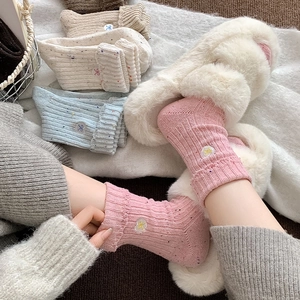 Close-up of thick knit wool socks featuring heart and bow embroidery with ribbed texture