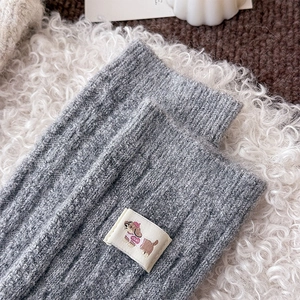 Detail of grey cable knit wool sock featuring a cute cartoon dog woven label and texture
