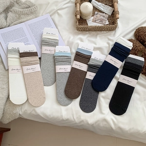 Flat lay of multiple color ribbed mid-calf socks on a cozy bed sheet with props