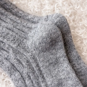 Close-up of grey ribbed wool socks with thick knit texture on a cozy white plush surface