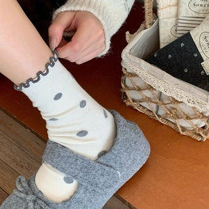 Close-up of beige crew socks with dark grey polka dots and ruffled edge design