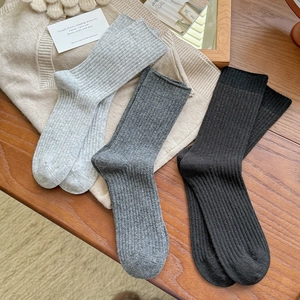 Three pairs of warm ribbed wool crew socks in grey and black on a wooden background