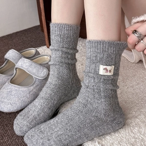 Detail of light gray cable knit wool socks featuring a cute dog patch on the side