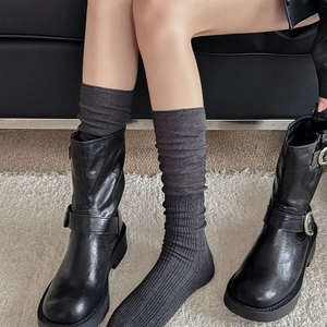 Eleganti calze grigie a coste indossate con stivali in pelle nera su tappeto bianco