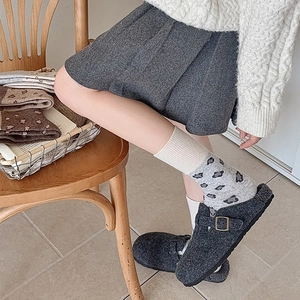 Close-up of grey felt clogs with metal buckle paired with heart pattern socks