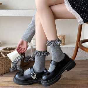 Dettaglio calzini grigi con pizzo a quadretti e fiocco abbinati a scarpe Mary Jane nere