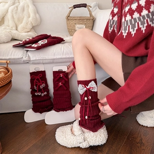 Detail of red knit leg warmers with white lace bows and ruffled edges for winter