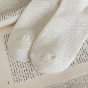 Detailaufnahme der cremefarbenen Wollsocken mit vertikaler Textur auf gemütlichem Buch