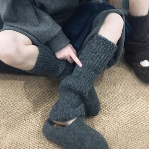 Close-up of grey cable knit leg warmers paired with cozy felt slippers on a soft carpet