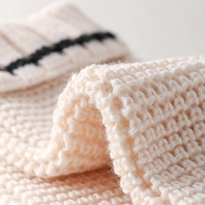 Macro shot of cream knit leg warmers showing wavy thick texture and black stripes