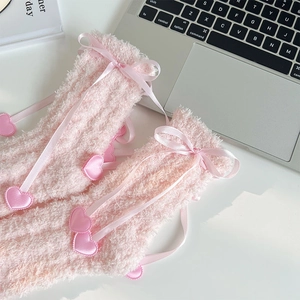 Gros plan de chaussettes en molleton corail rose avec nœuds et breloques cœur 3D