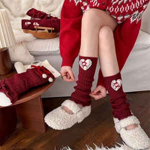 Macro detail of red cable-knit leg warmer with heart patch and lace ribbon bow
