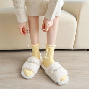 Détail de chaussons en peluche blancs et chaussettes en polaire corail à nœuds