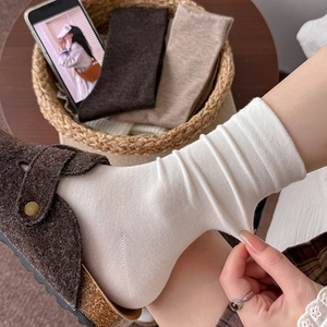 White ribbed knit crew socks styled with brown slippers in a cozy home setting