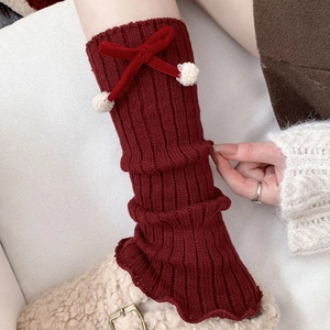 Detail of red cable-knit leg warmers with velvet bows and white faux fur pom-poms