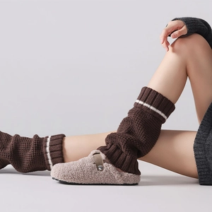 Close-up of brown knit leg warmers with white stripes paired with oatmeal plush mules