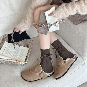 Close-up of knit socks with leopard bow details and suede clogs in a cozy home setting