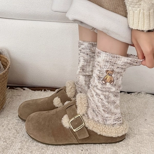 Close-up of brown suede slippers with plush lining and bear embroidery knitted socks