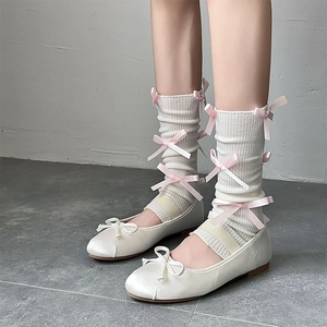 Detail of white knit leg warmers with pink ribbon bows and satin ballet flats