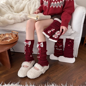 Detail of burgundy knit leg warmers with white lace bows and plush pompom accents
