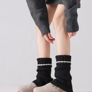 Detailed knit texture of thick black leg warmers featuring a white stripe and ribbed cuffs